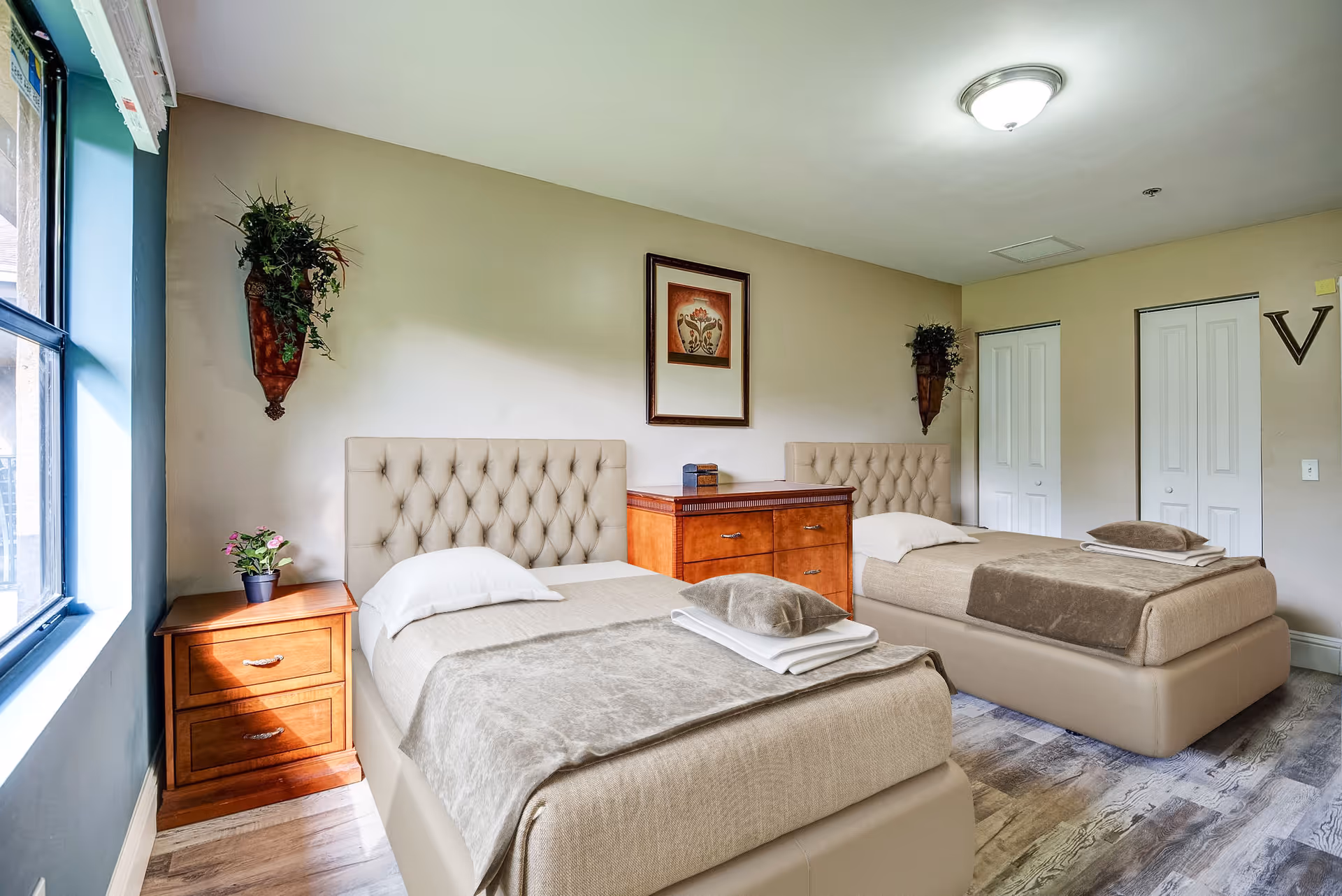 Two twin beds with tufted headboards, a wooden dresser, and nightstands in a bright bedroom.