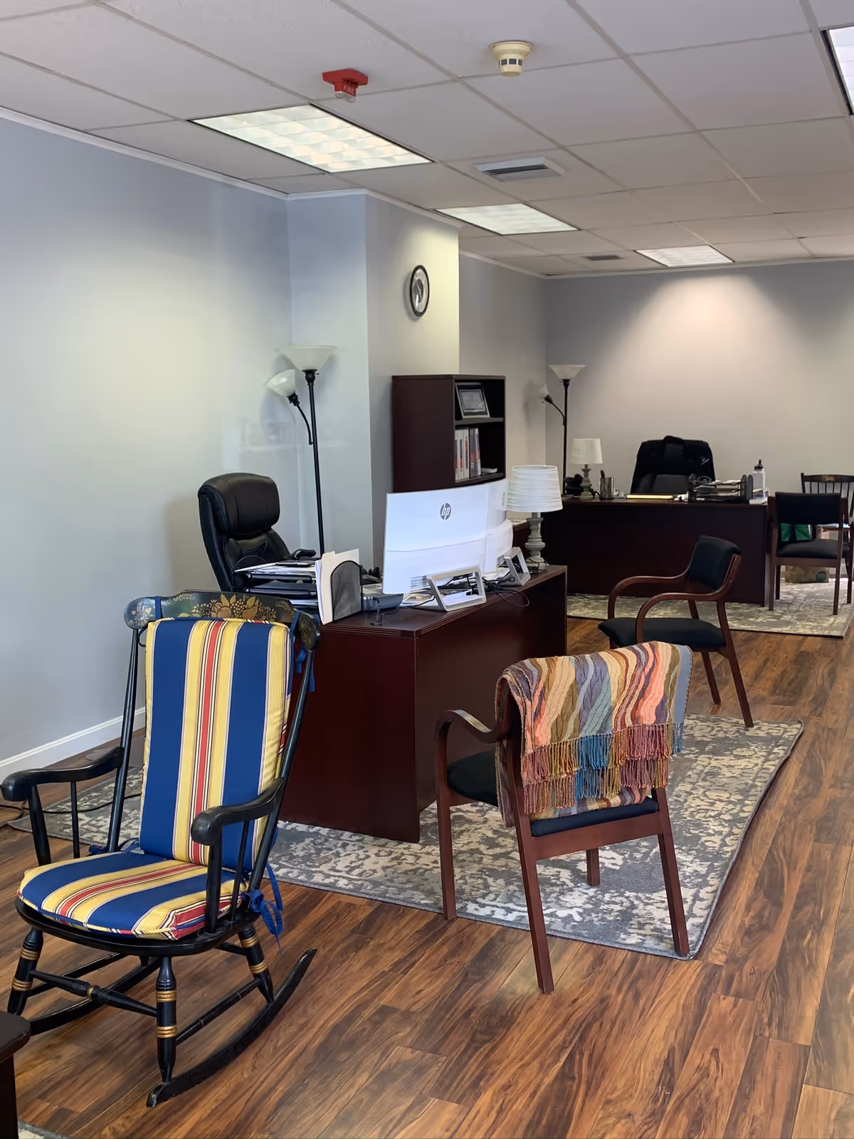 Office reception area with desk, computer, seating, lamps, and striped rocking chair.