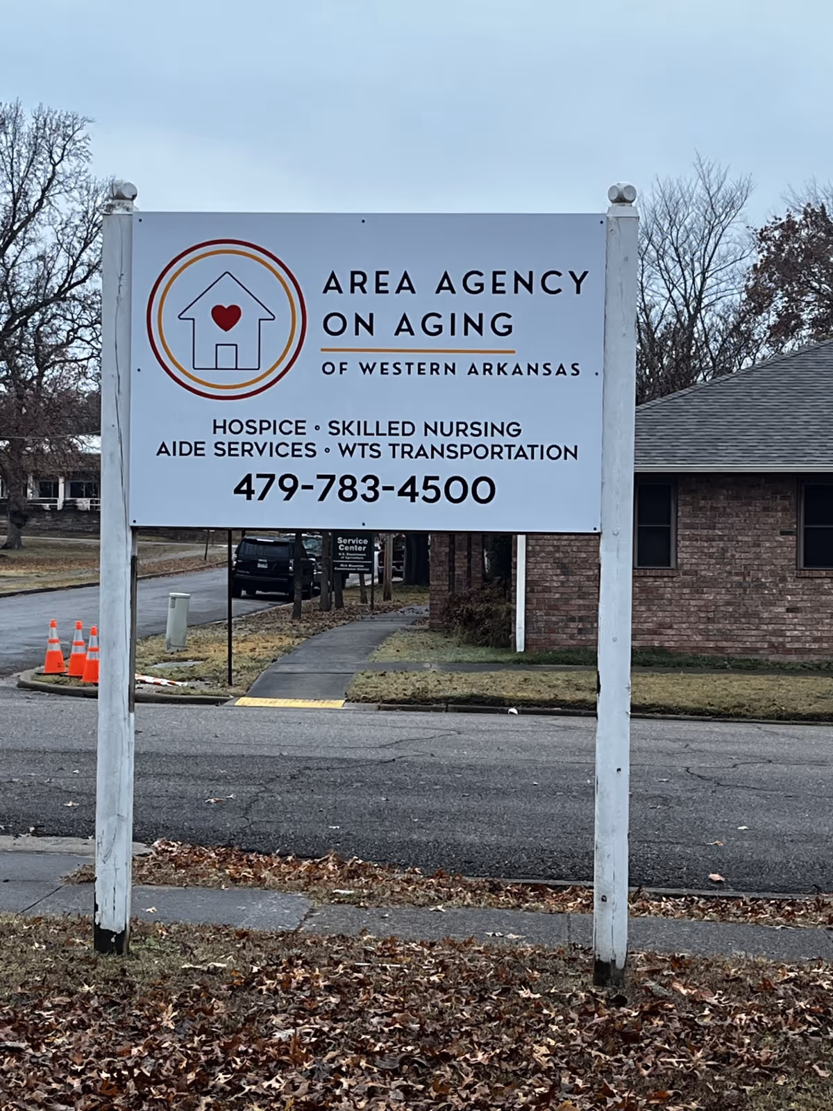 A white sign for Area Agency On Aging stands on posts near a brick building.