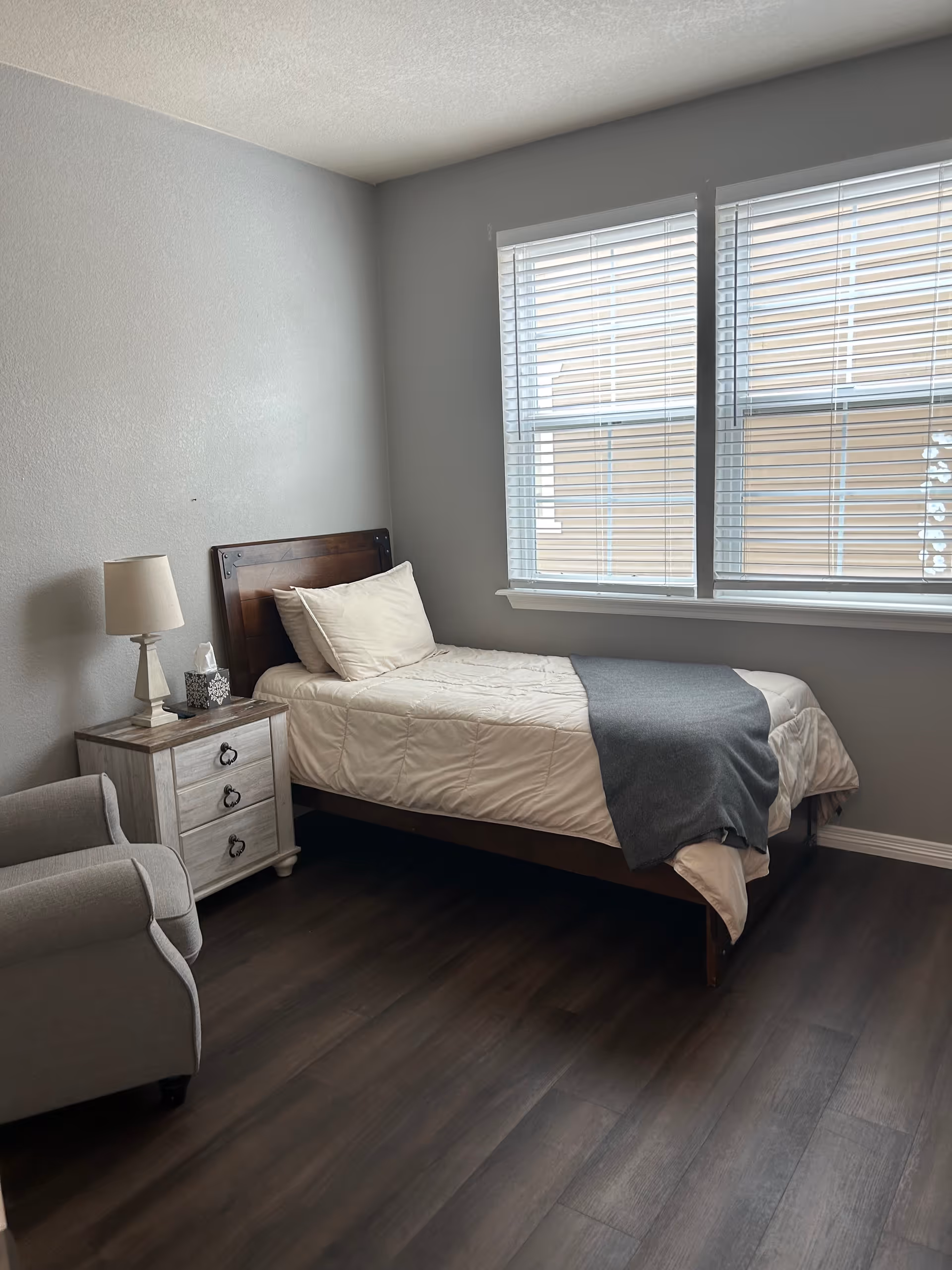 A clean bedroom in a senior living facility with a single bed and nightstand.
