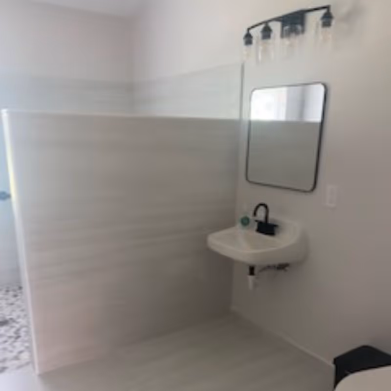 Small bathroom with sink, mirror, and partial partition wall.