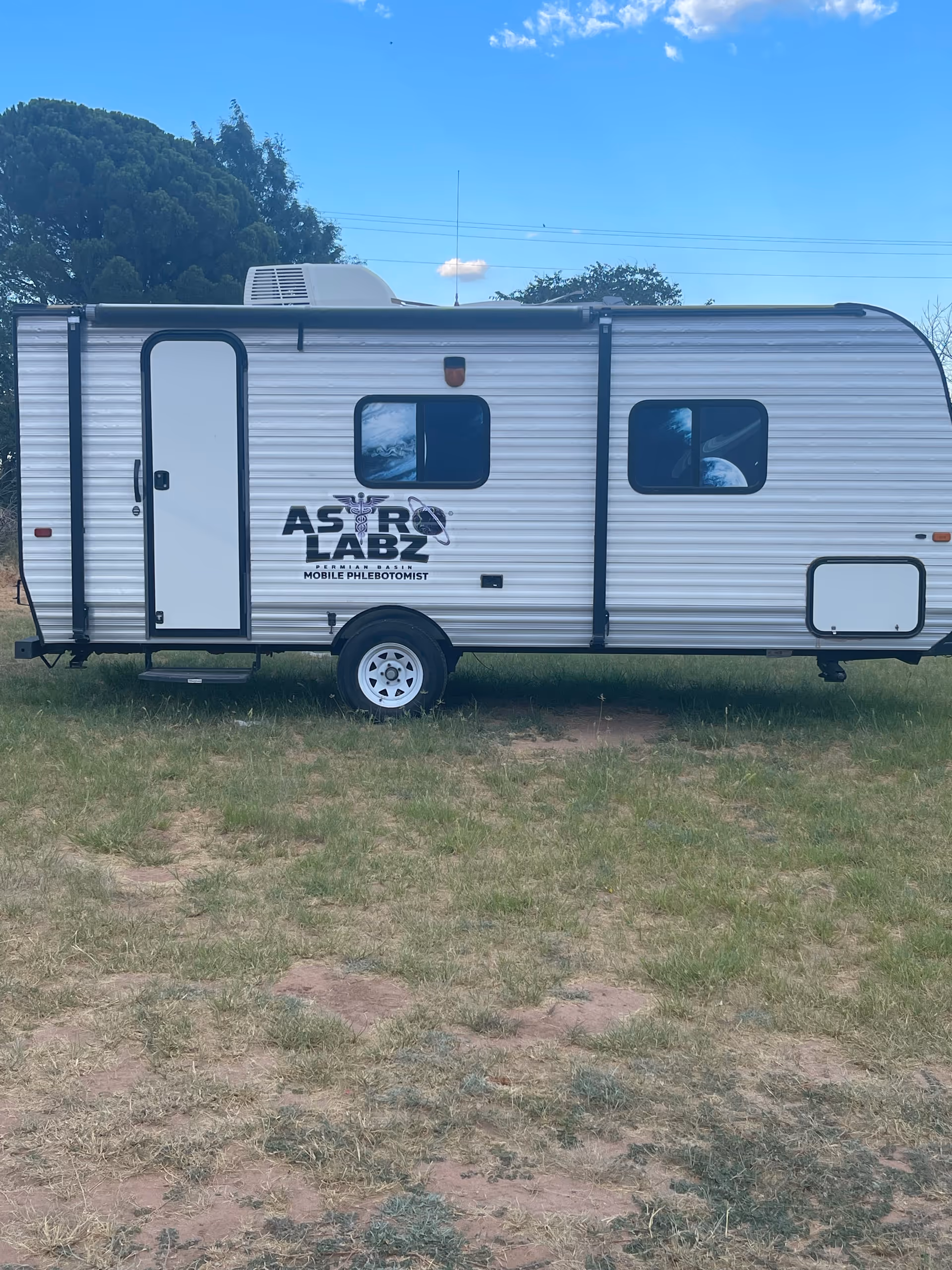 A white mobile lab trailer labeled Astro Labz Permian Basin parked on a grassy field.
