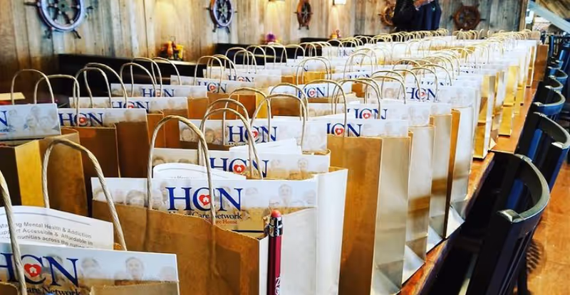 Row of brown gift bags lined up on a long indoor conference table.