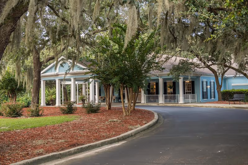 Blue senior living facility entrance with white columns and a curved driveway.