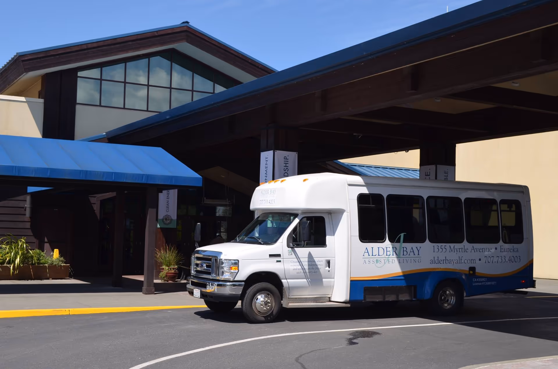 White shuttle bus parked at the entrance of Alder Bay Assisted Living building.