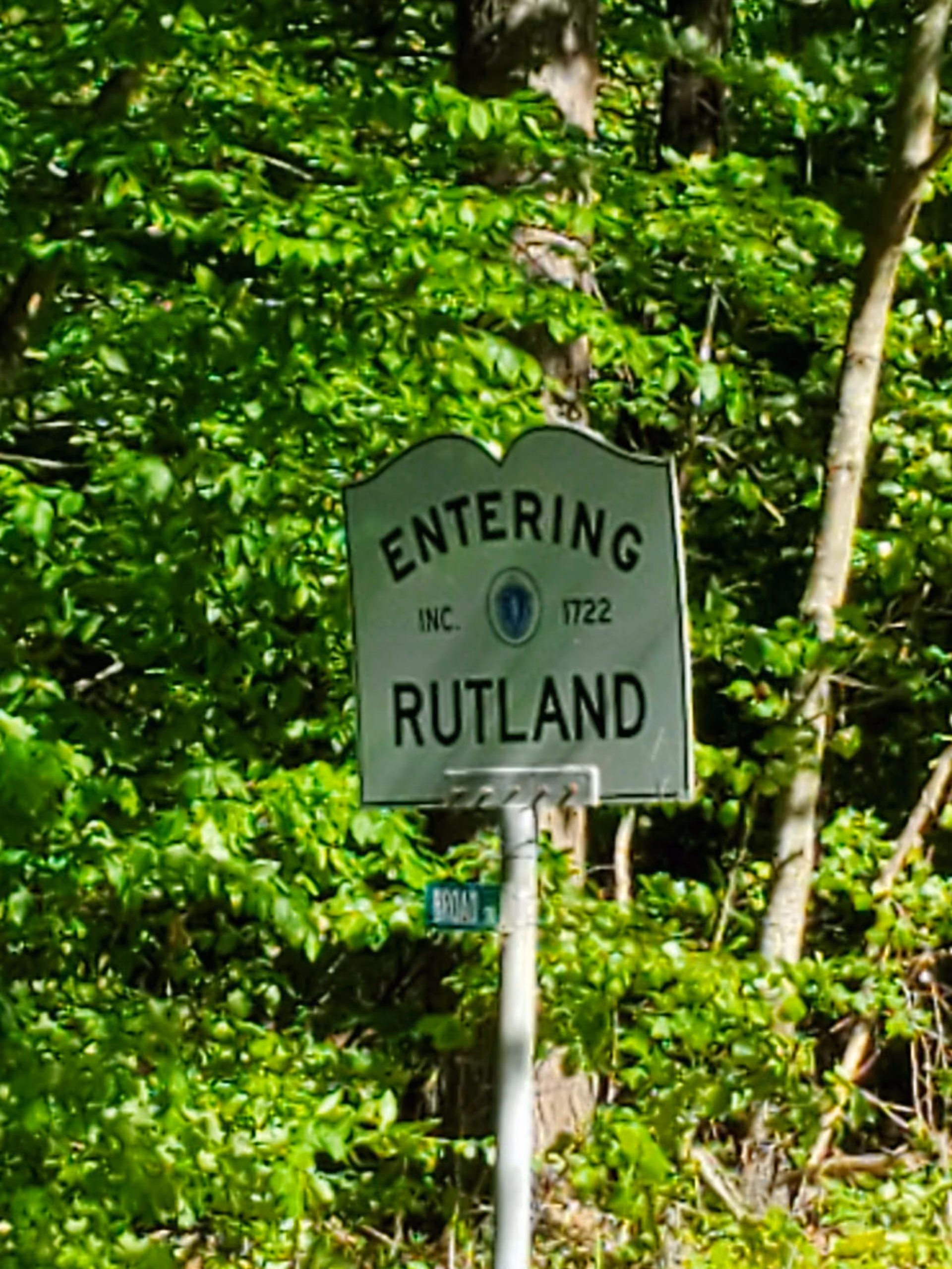 A street sign reading 'Entering Rutland' surrounded by dense green trees