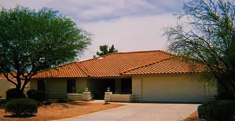 Single-story stucco house with a red tile roof, attached garage, driveway, and desert landscaping.