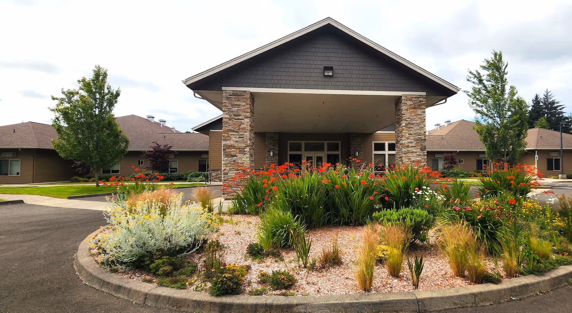 Exterior view of a memory care facility entrance with a landscaped circular garden.