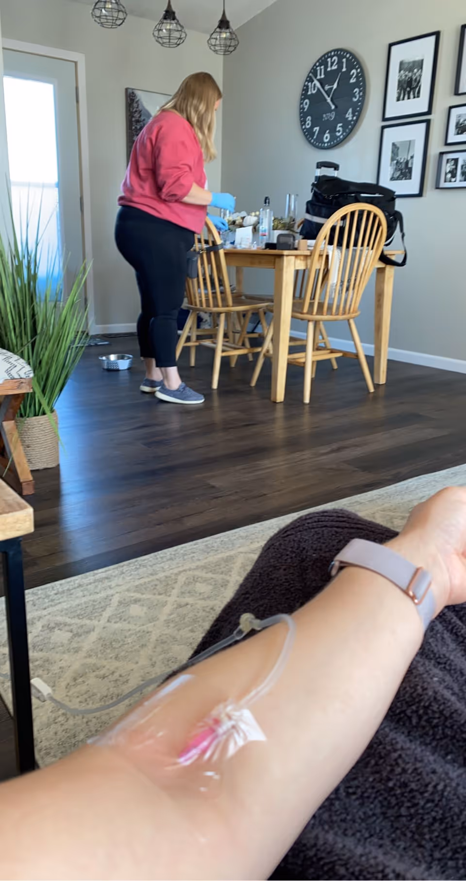 Caregiver with gloves prepares items at a wooden dining table, while an IV arm is visible.
