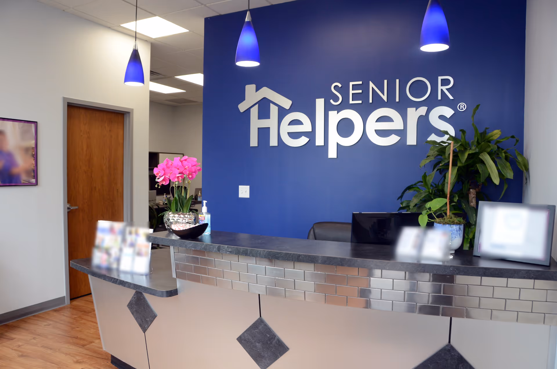 Reception desk in a modern lobby with blue wall and Senior Helpers logo.