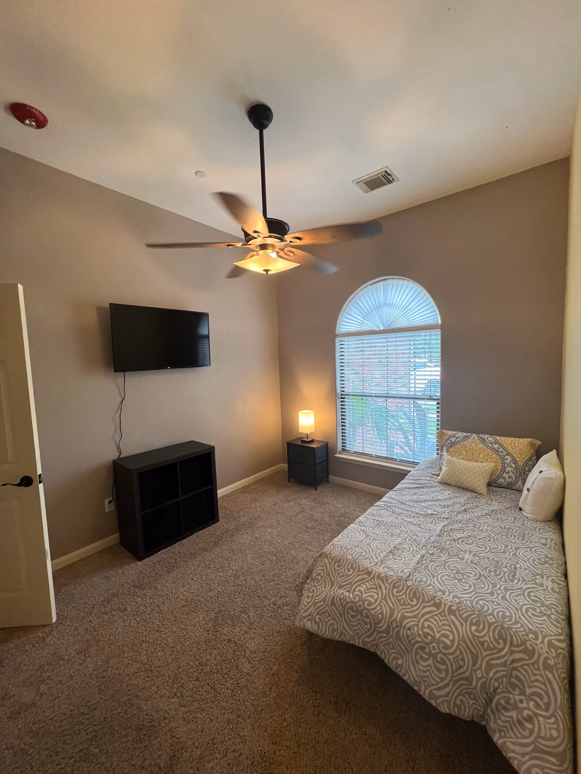 Cozy bedroom with bed, window, nightstand, TV, and ceiling fan.