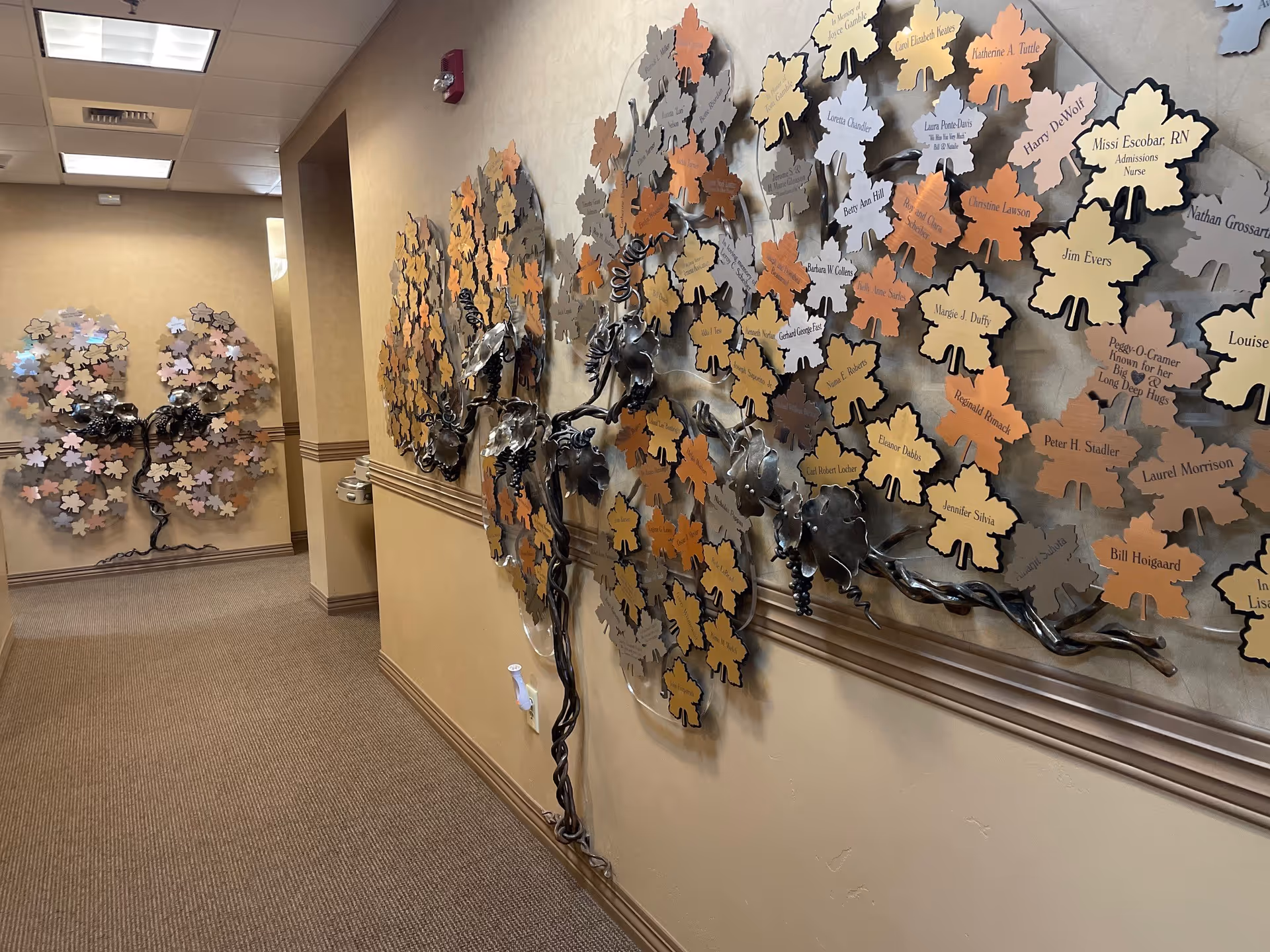 Interior hallway with colorful leaf wall art and a metal tree sculpture along the corridor.