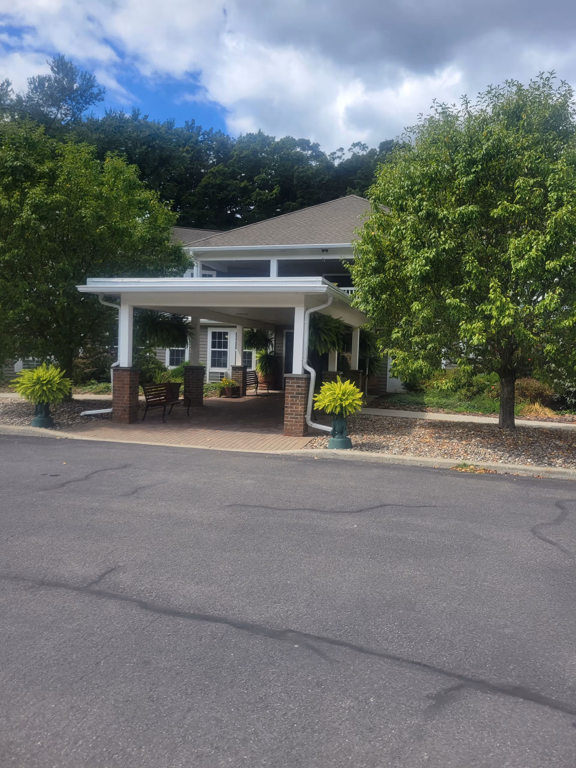 Entrance to Mountain Valley Manor Adult Home with a covered drop-off, benches, and greenery.