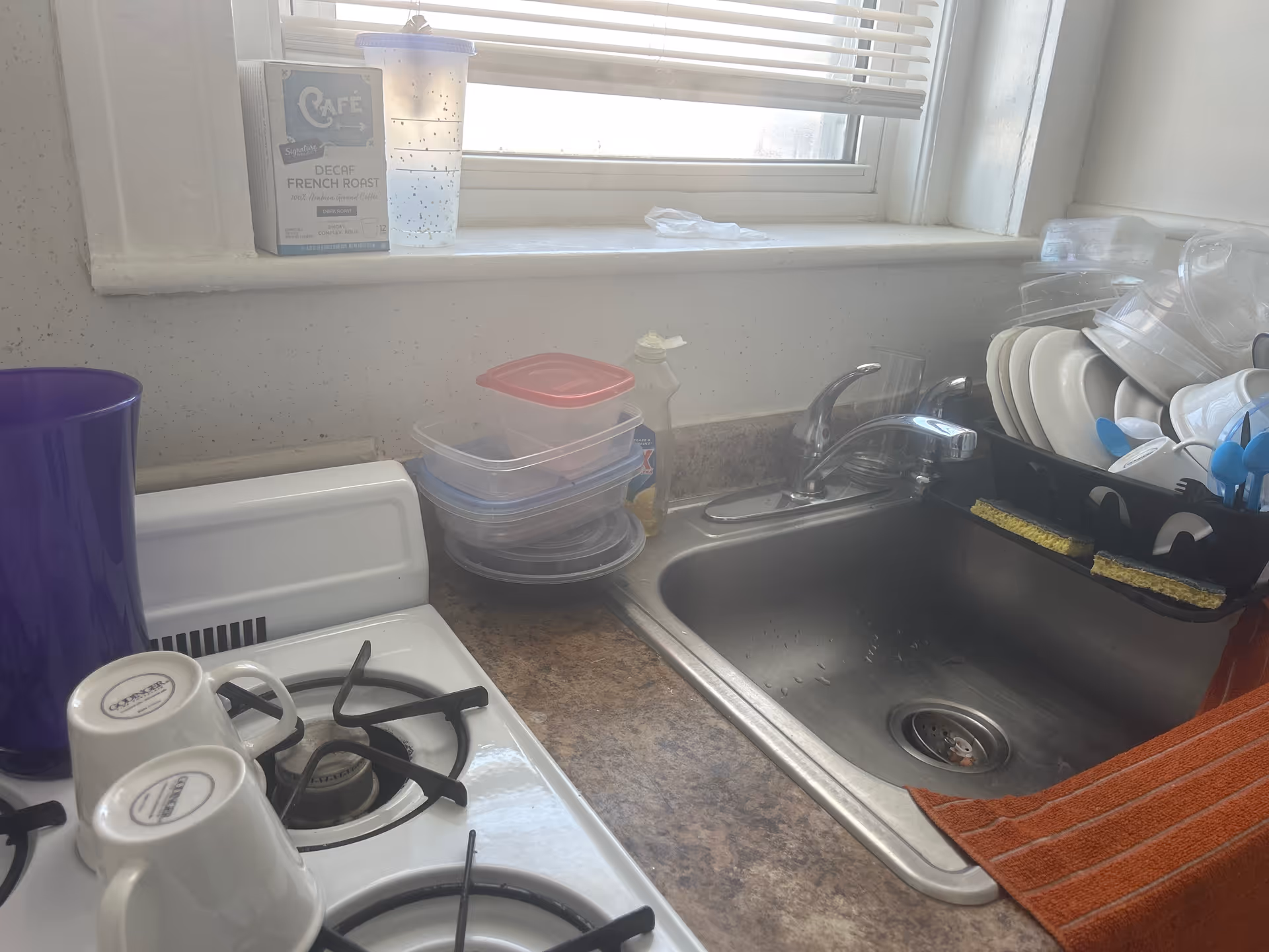 Kitchen counter with sink, stacked plastic containers, and dish rack by a window.