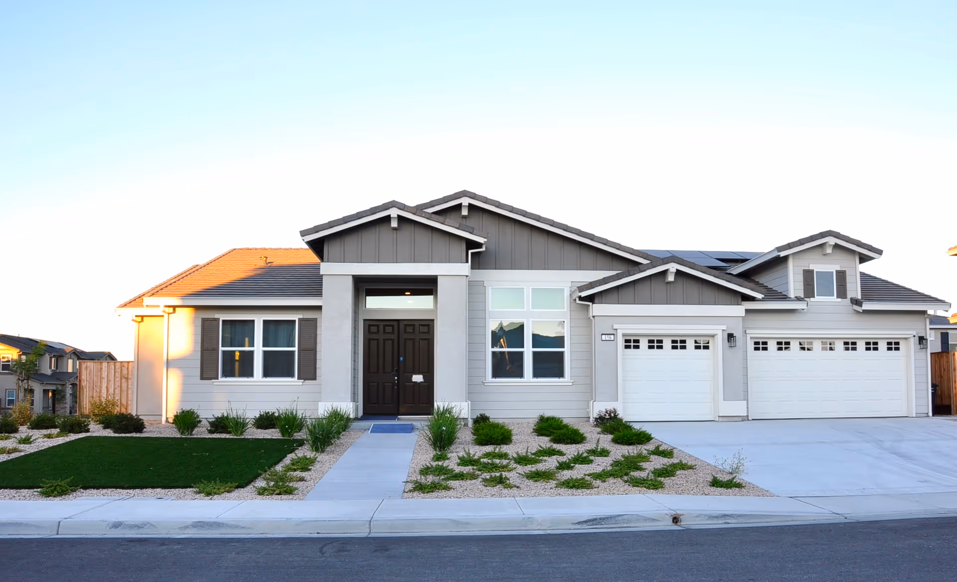 Front exterior view of a single-story modern house with a three-car garage, a dark brown front door, and a landscaped front yard with grass and small bushes.