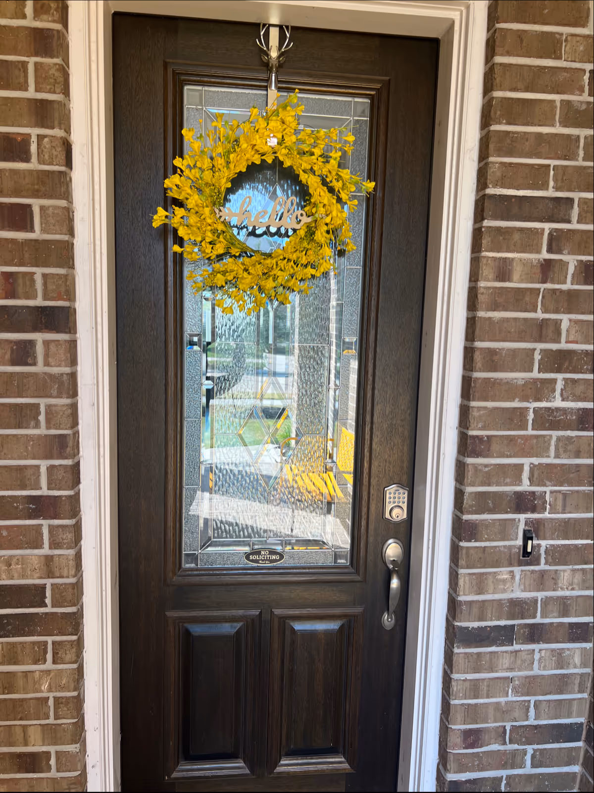 Front door with a yellow wreath on a brick exterior entryway.