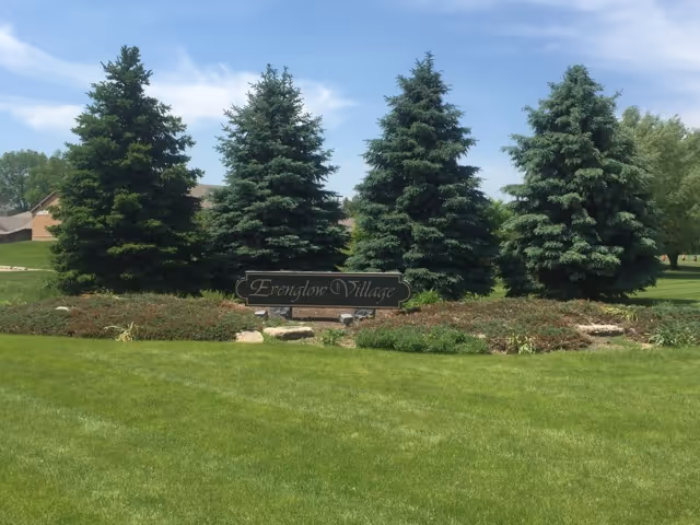 Well kept lawn with three evergreen trees and a sign reading Evenglow Inn at the entrance.