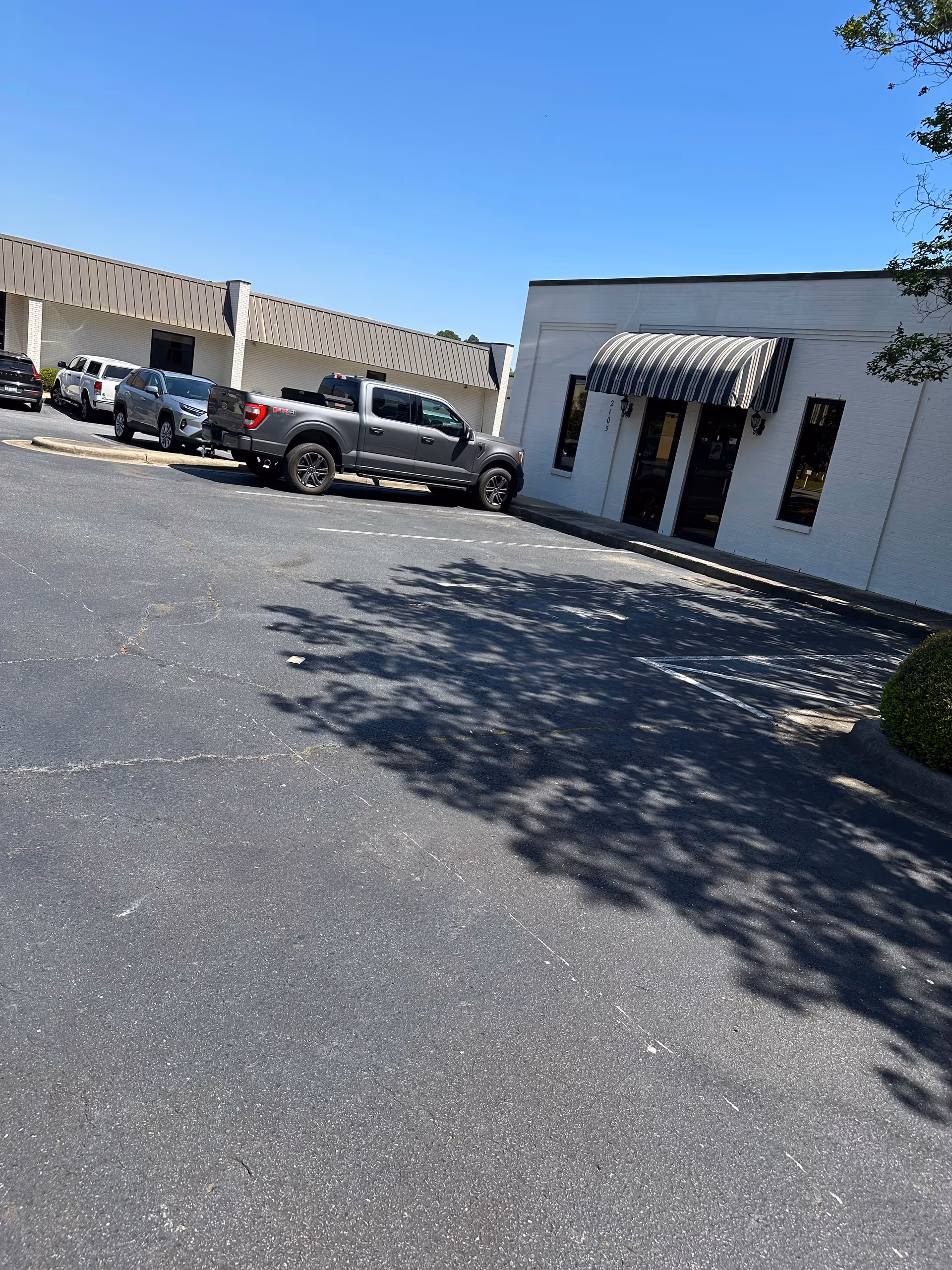 Exterior view of a white building with striped awning and parked vehicles in the lot.