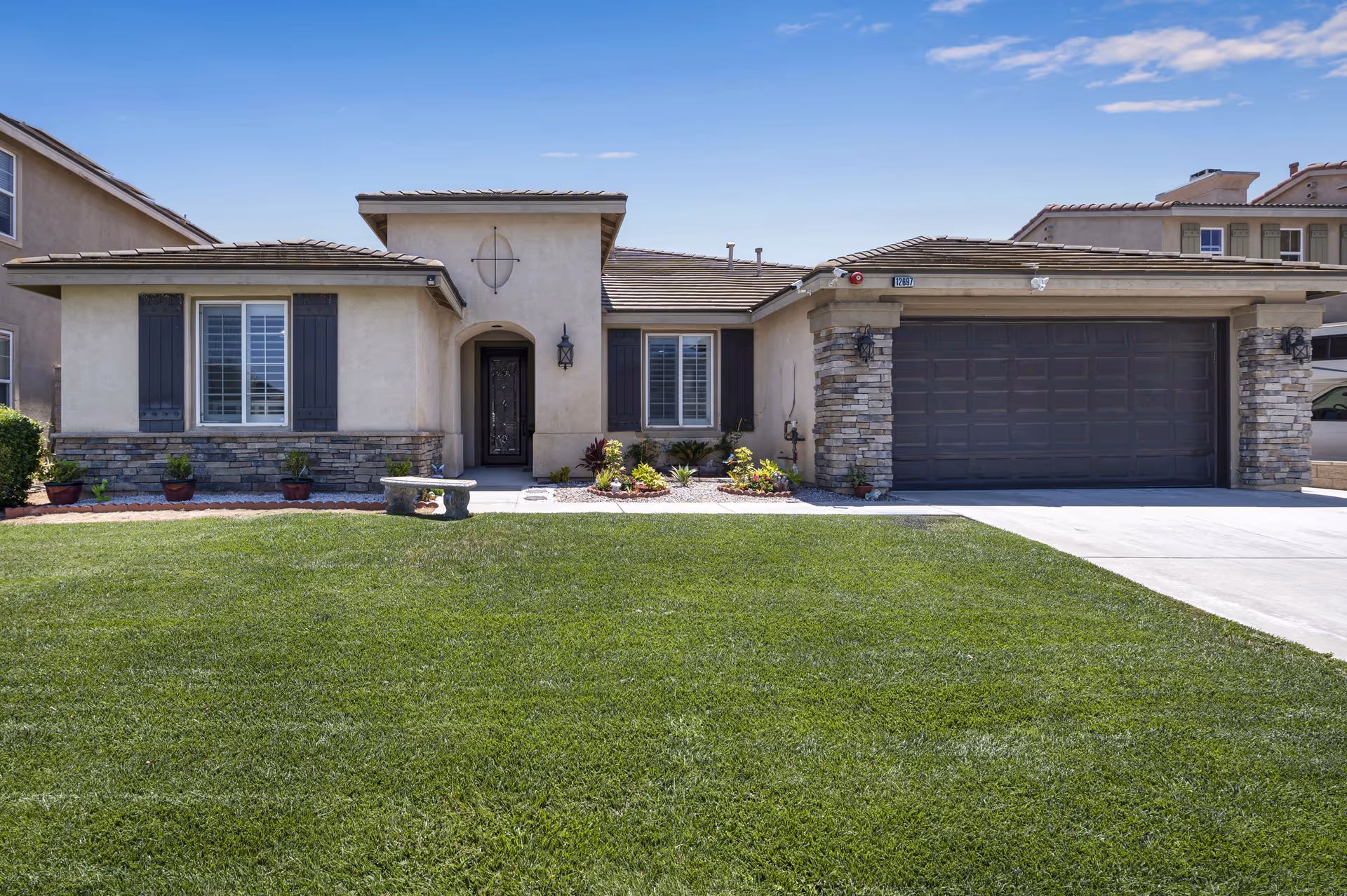Front exterior of a single-story residence with stone accents, a two-car garage, and a manicured lawn.