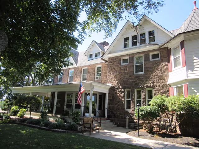 Front exterior view of Pickering Manor with stone facade, porch, flag, and surrounding trees.
