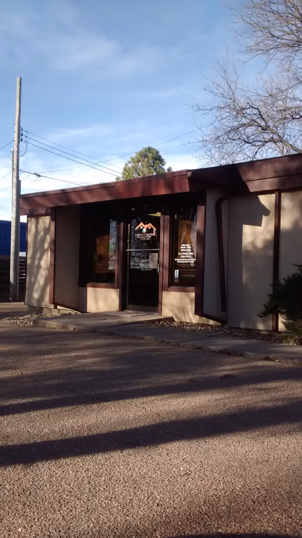 Front exterior of a small beige building with maroon trim and glass entrance.