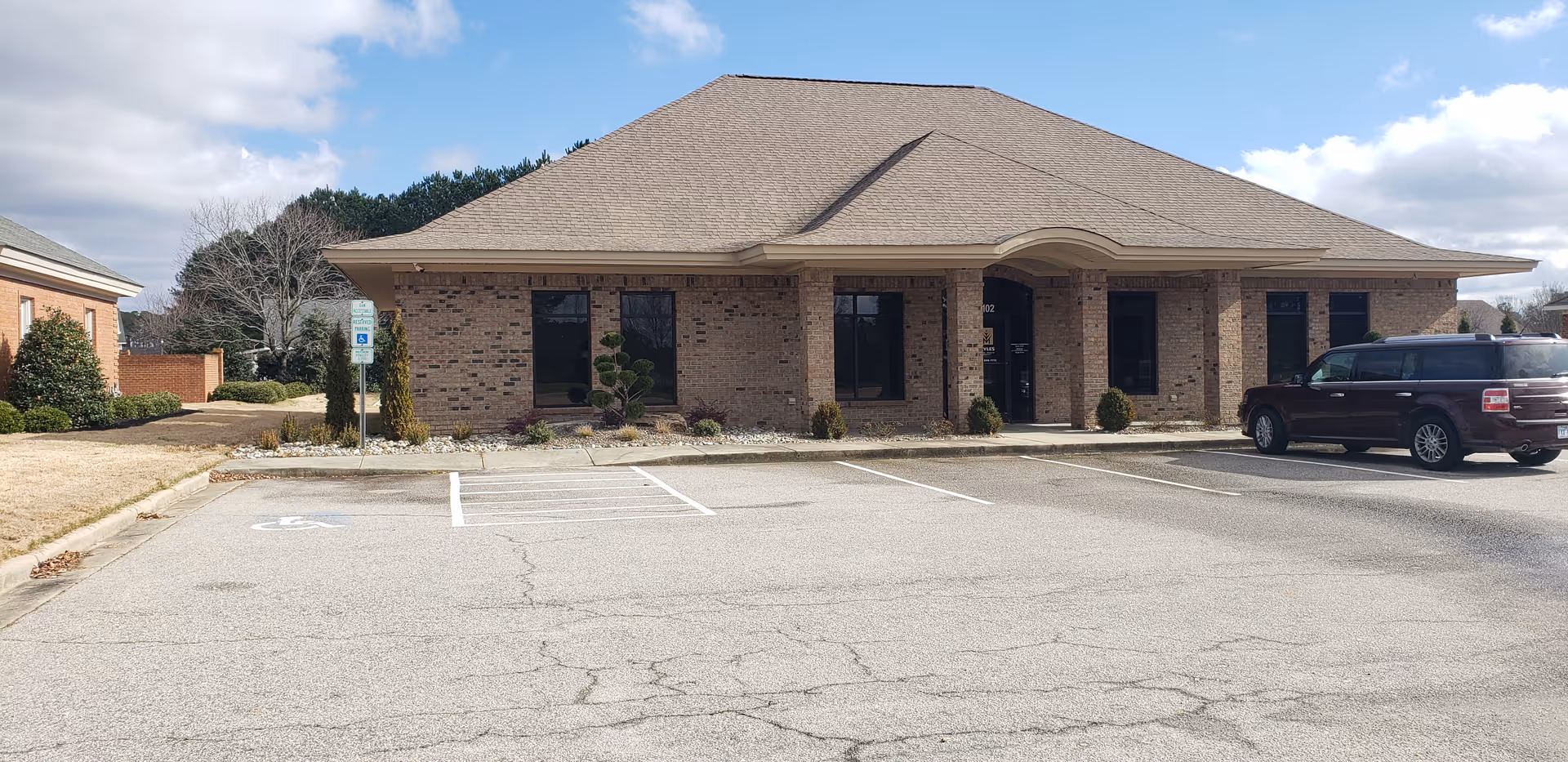 Single-story brick facility with a curved entrance arch, parking lot, and wheelchair accessible signage.