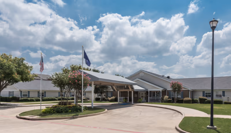 Exterior view of Arden Courts Of Richardson with a covered entrance, flags, and landscaped circle drive.