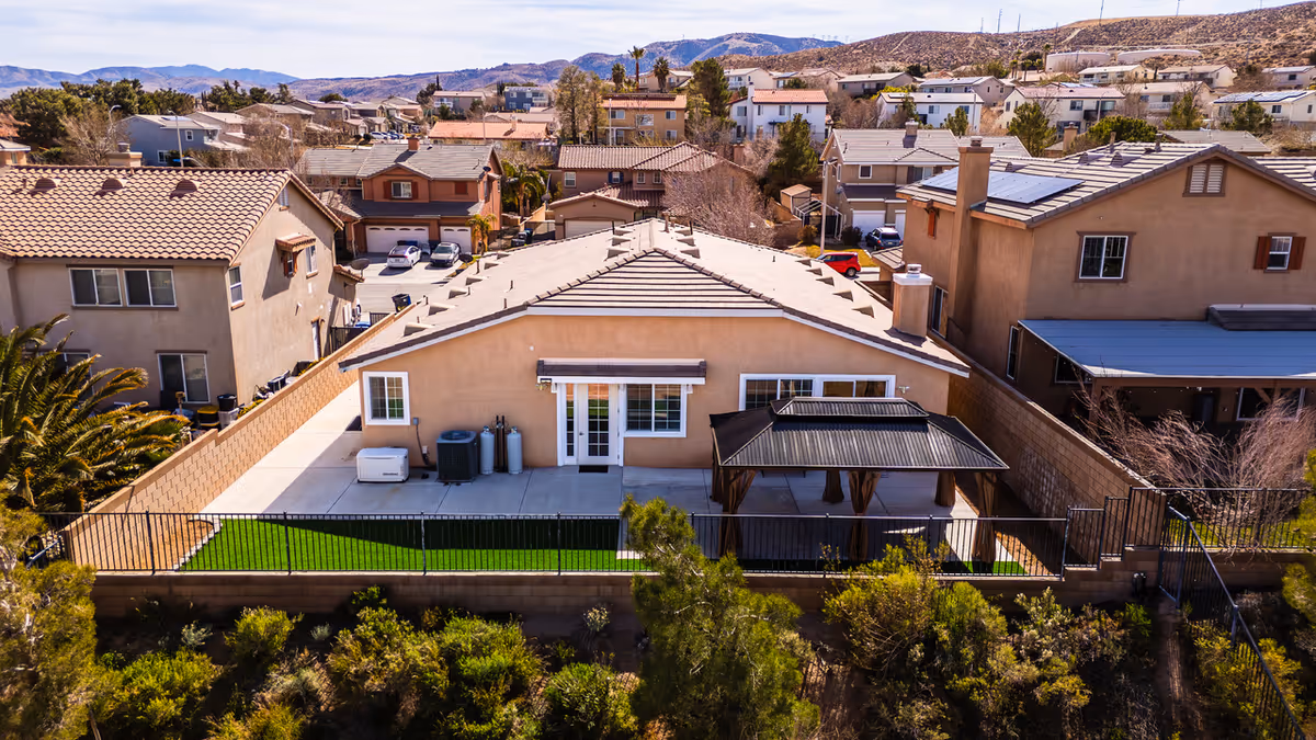 Residential exterior with a fenced backyard, patio, and neighboring houses in a sunny neighborhood.