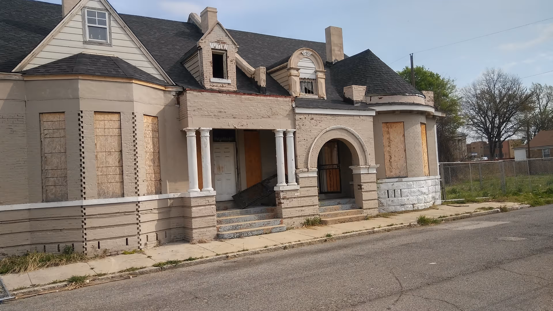 Dilapidated, boarded-up building with a stone porch and arched entry on a desolate street.