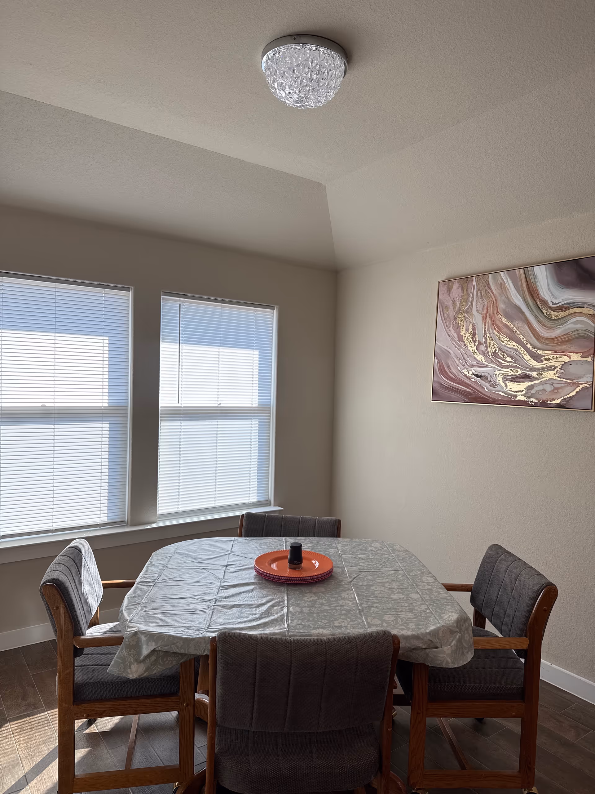 A small dining room with a table, chairs, blinds, and abstract wall art.
