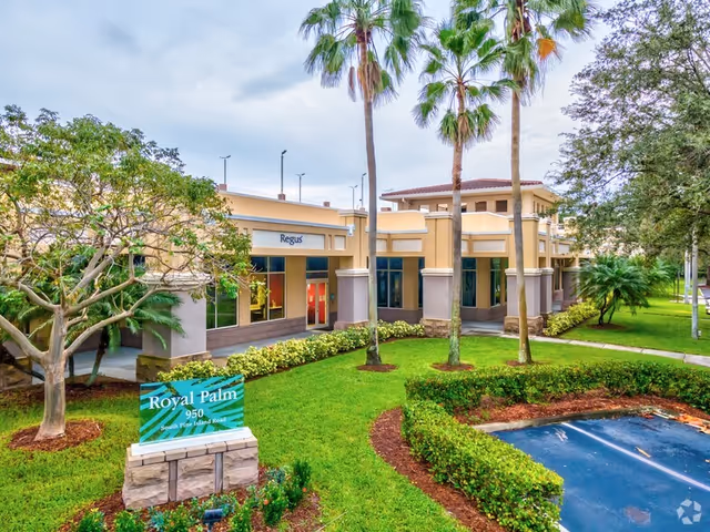 Senior living facility exterior with palm trees, lawn, and entry sign.