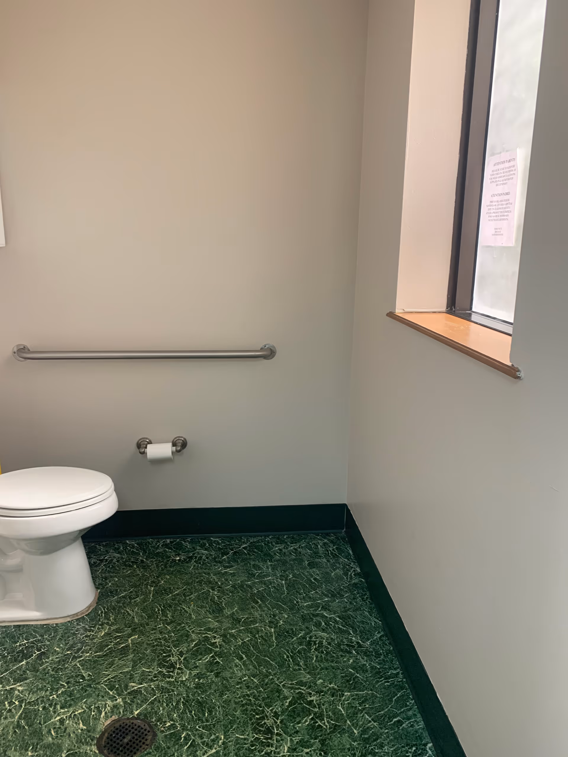 Small bathroom with a toilet, grab bar, window, and green tiled floor.