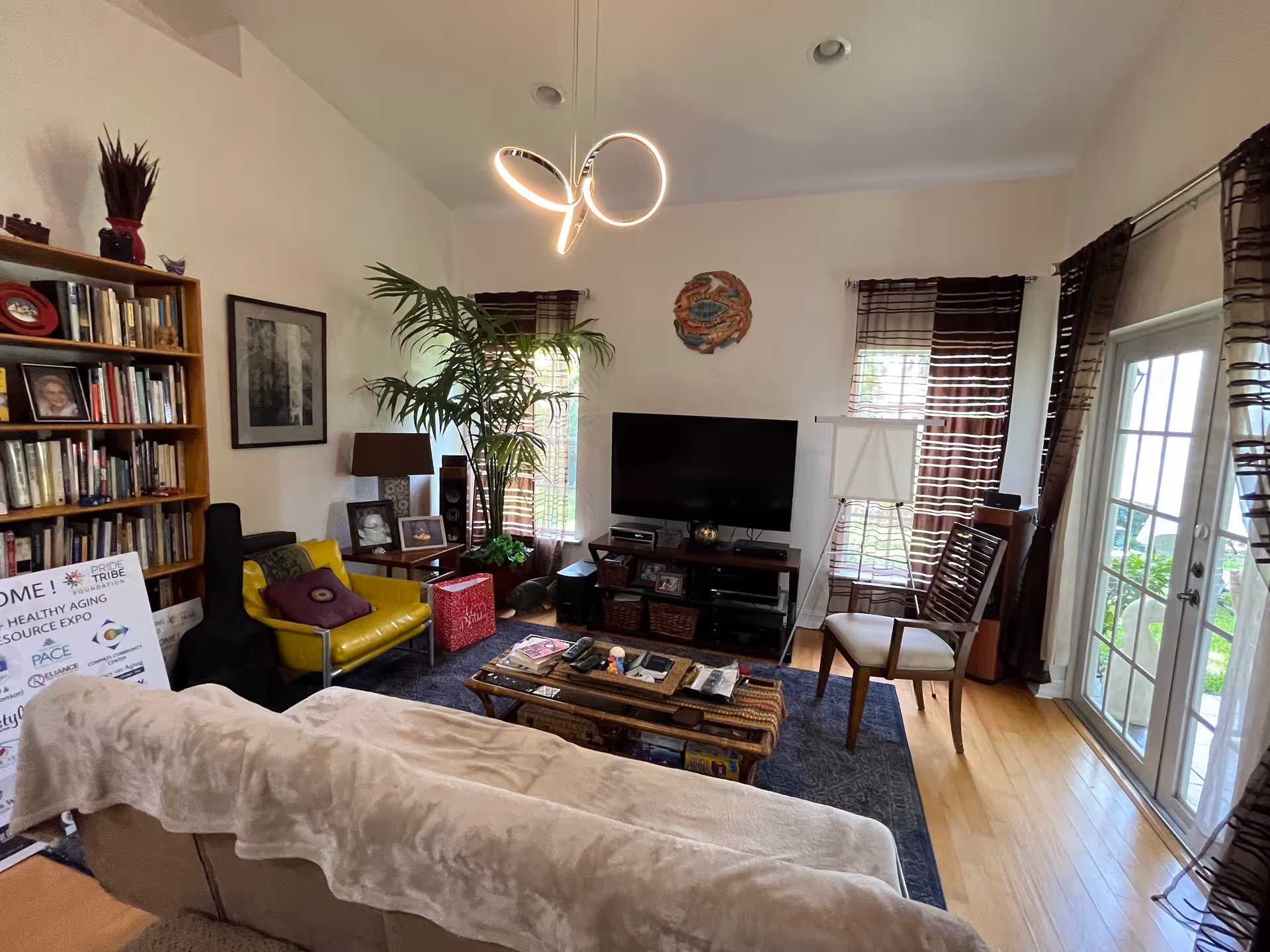 Cozy living room with sofa, chairs, coffee table, TV, shelves, and plants.