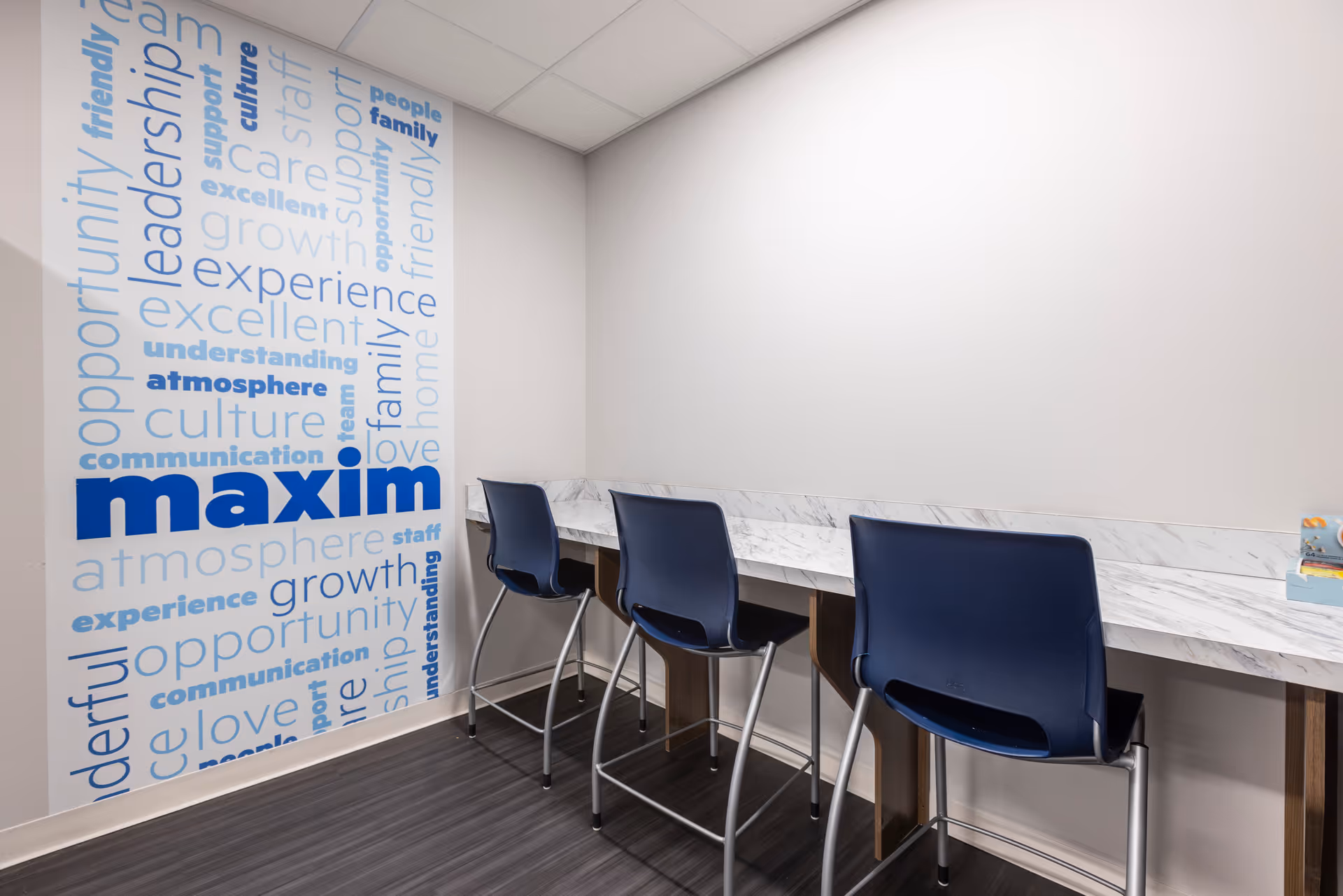 Interior office area with marble counter, blue chairs, and a wall mural reading maxim.
