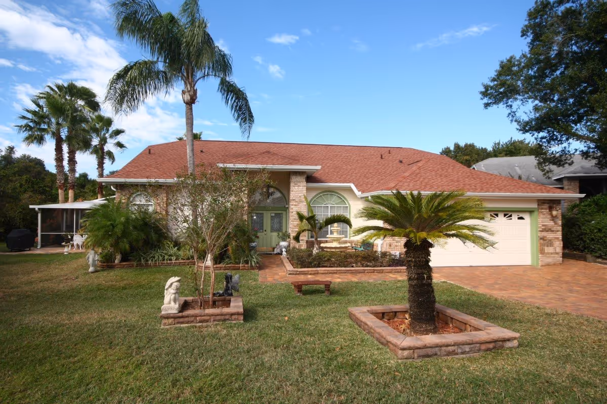 Single-story house with red roof, green front door, and palm trees in a landscaped front yard.