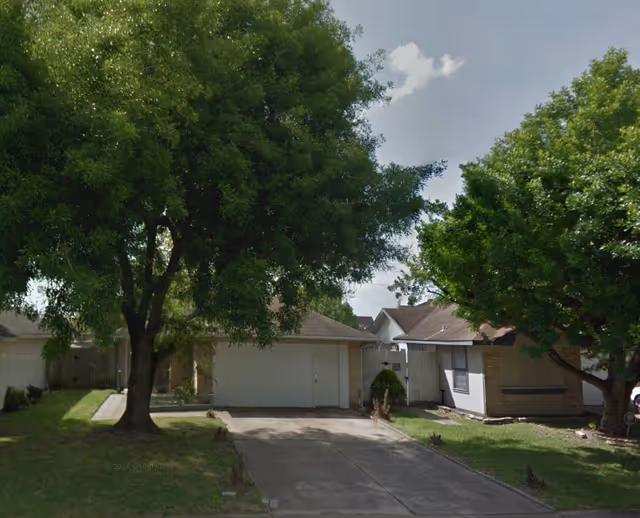 Exterior view of a residential street with two garages and large trees.