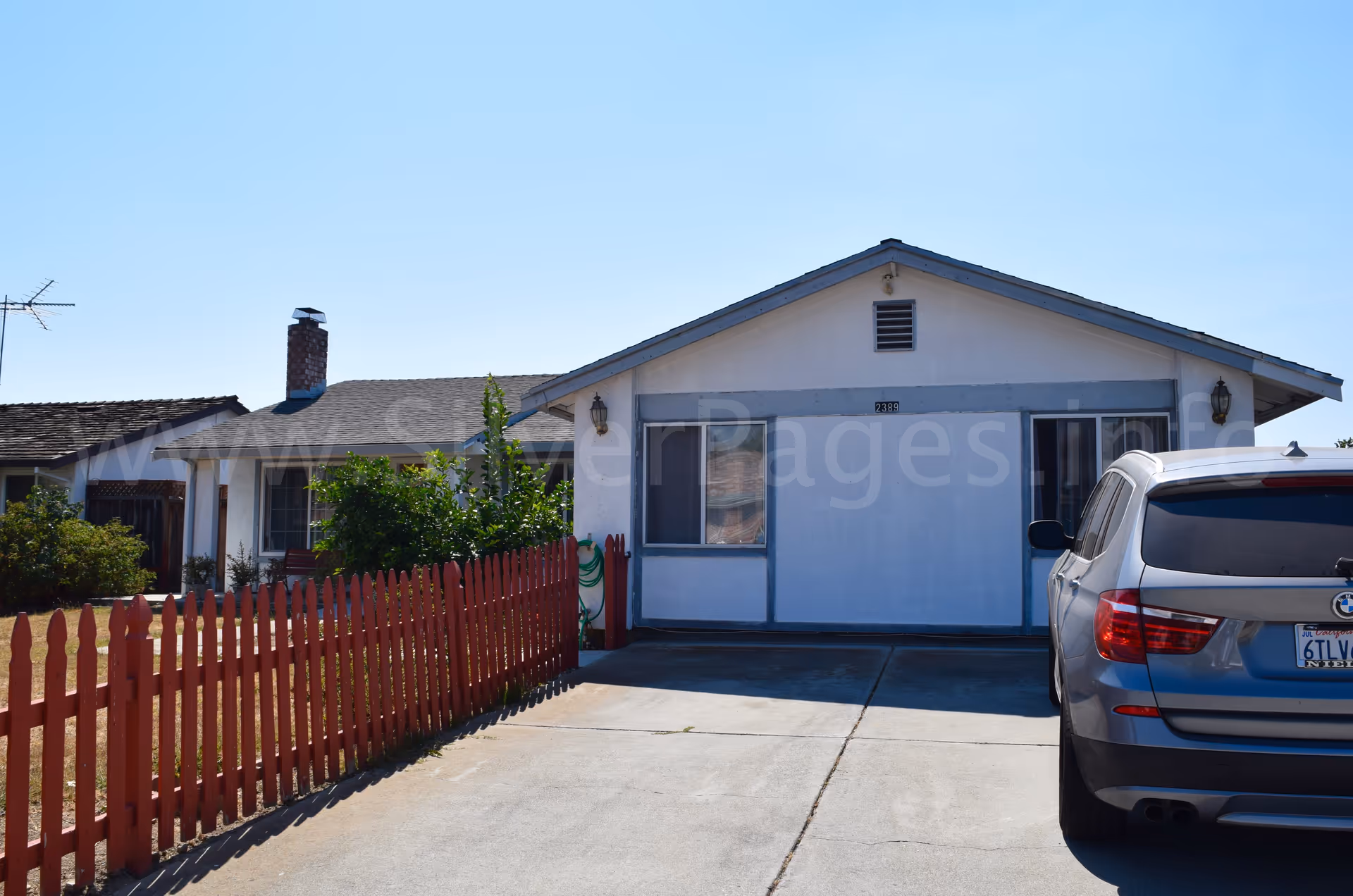 Front exterior of a single-story house with a red picket fence and car in driveway.