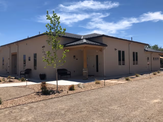 A single-story beige senior living facility exterior with a small porch and desert landscaping.