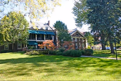 Lush lawn and trees frame a brick senior living facility with a shaded porch.
