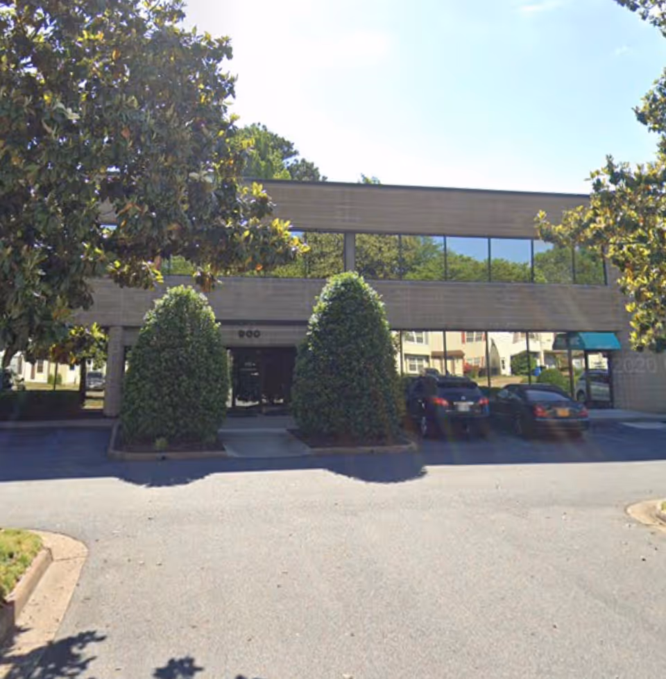 Exterior view of a two-story building with large windows, trees, and parked cars.