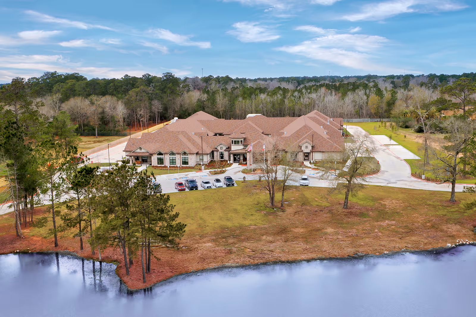 Exterior view of The Heights on Valley Ranch, a senior living campus with parking and pond.