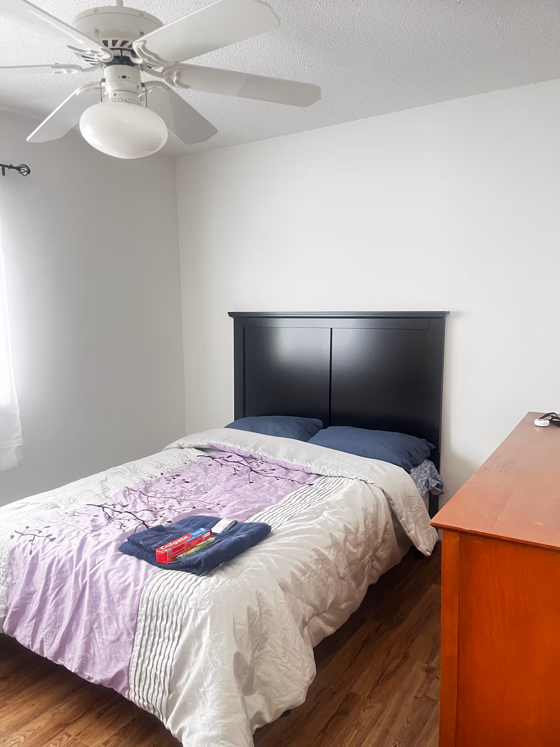 A tidy bedroom with a double bed, dark headboard, ceiling fan, and dresser.