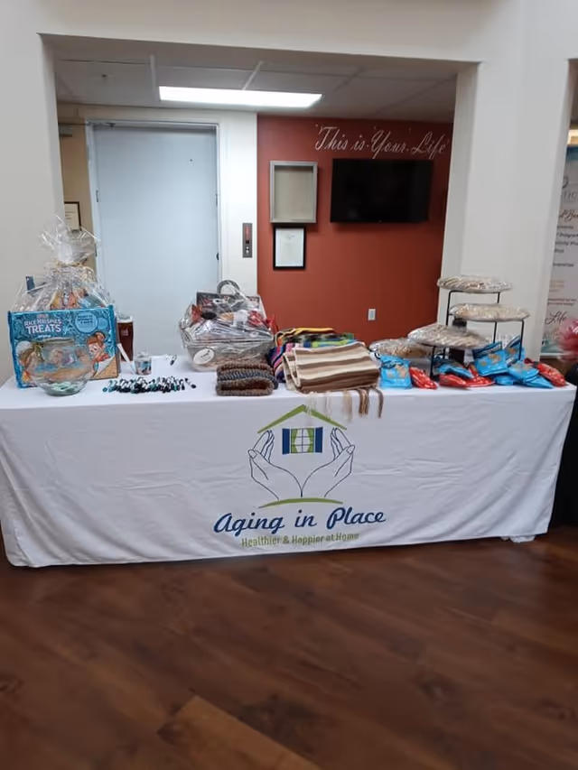 Indoor lobby table with Aging in Place logo displaying gifts, blankets, and decor.