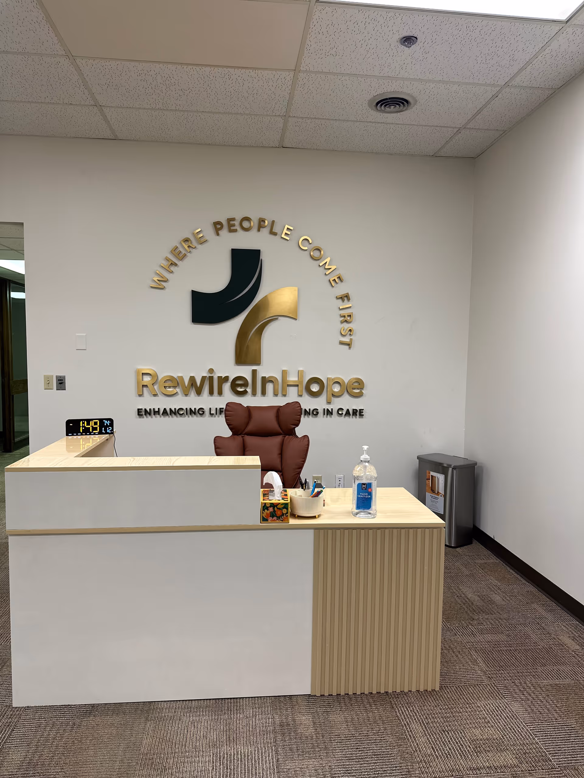 Reception desk in a lobby featuring RewireInHope logo and slogan on wall.