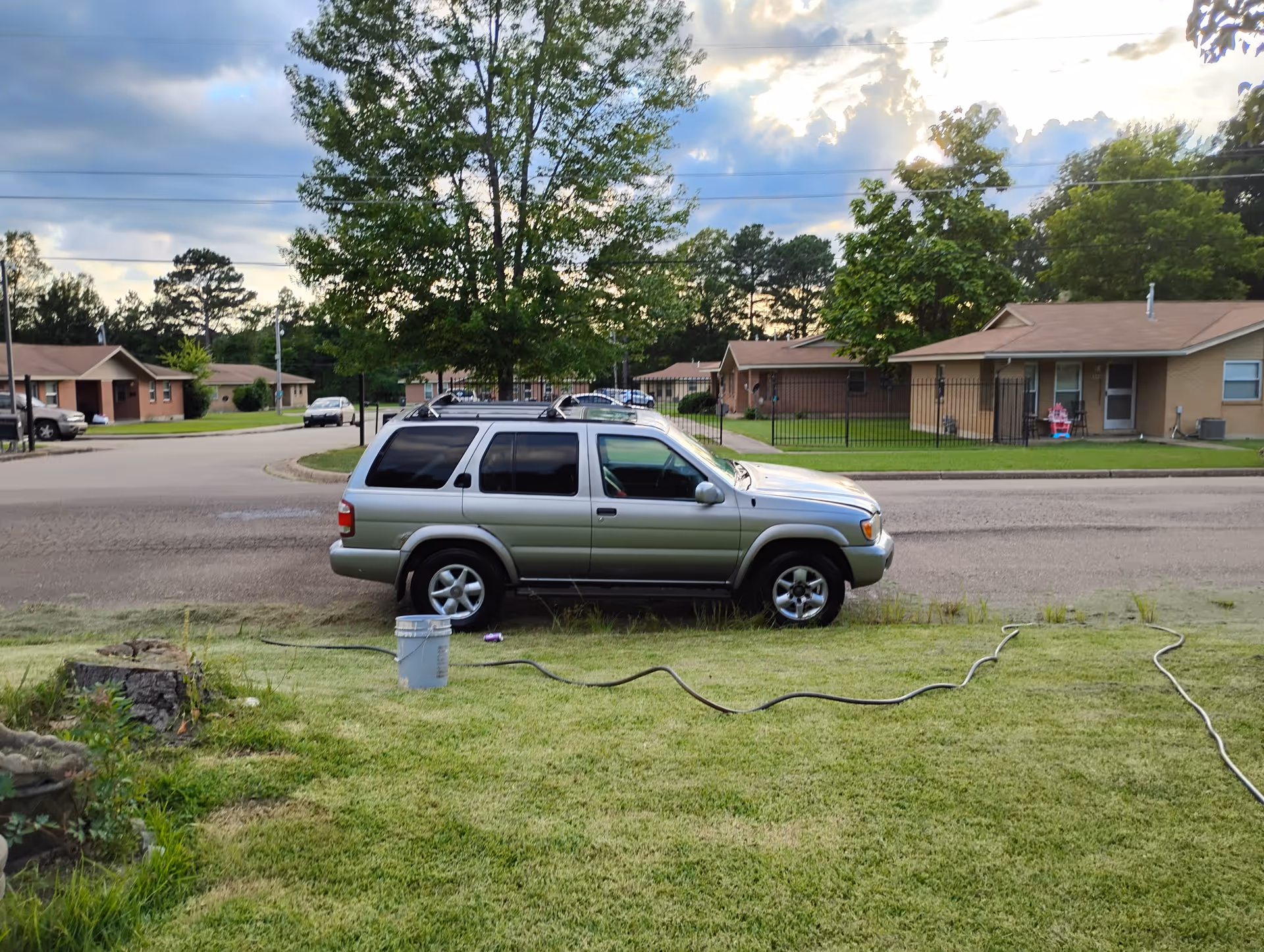 A silver SUV parked on a residential street with single-story houses and trees in the background.