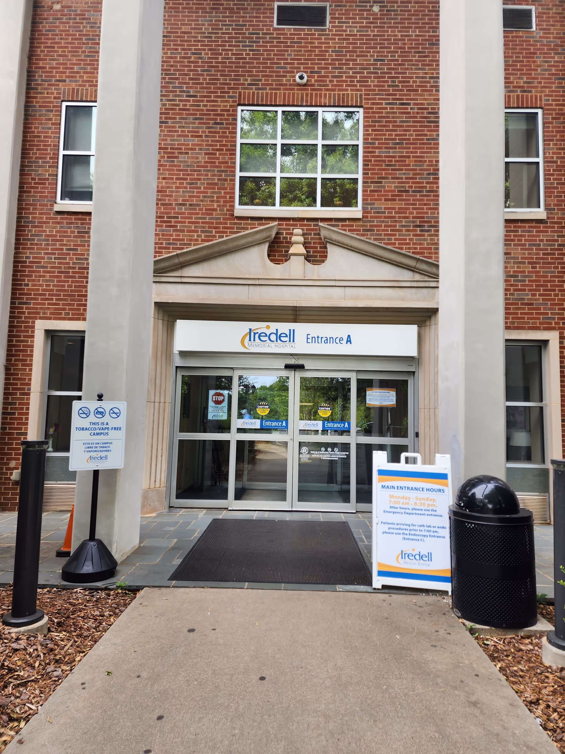Brick hospital entrance with glass doors reading Entrance A and Iredell signage, exterior view.