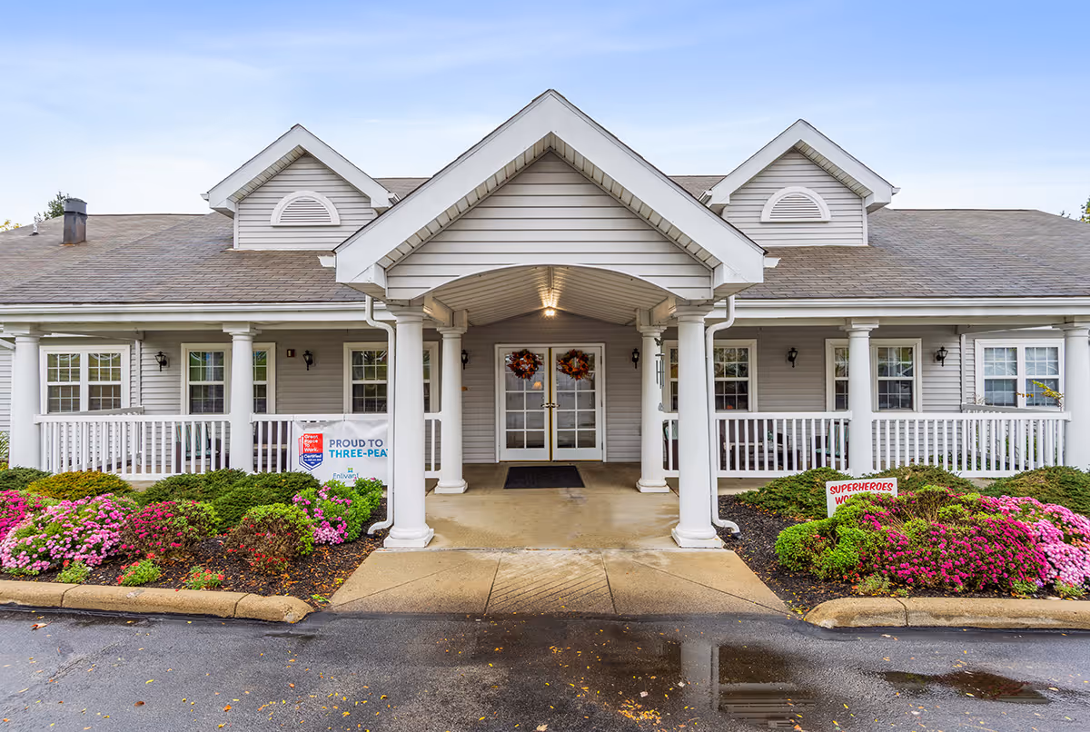 Front entrance of Allegheny Place senior living facility with white columns and blooming shrubs.