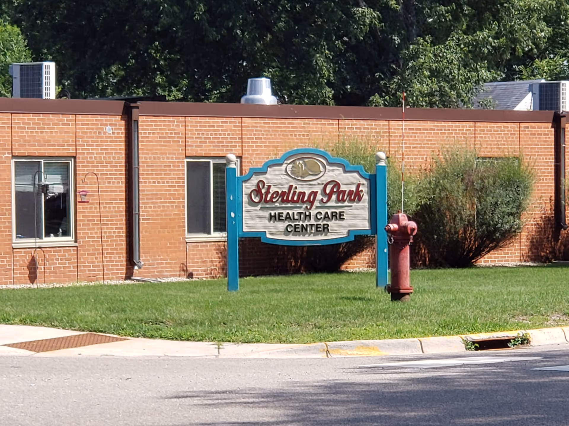 Brick exterior of Sterling Park Health Care Center with a sign and green lawn.
