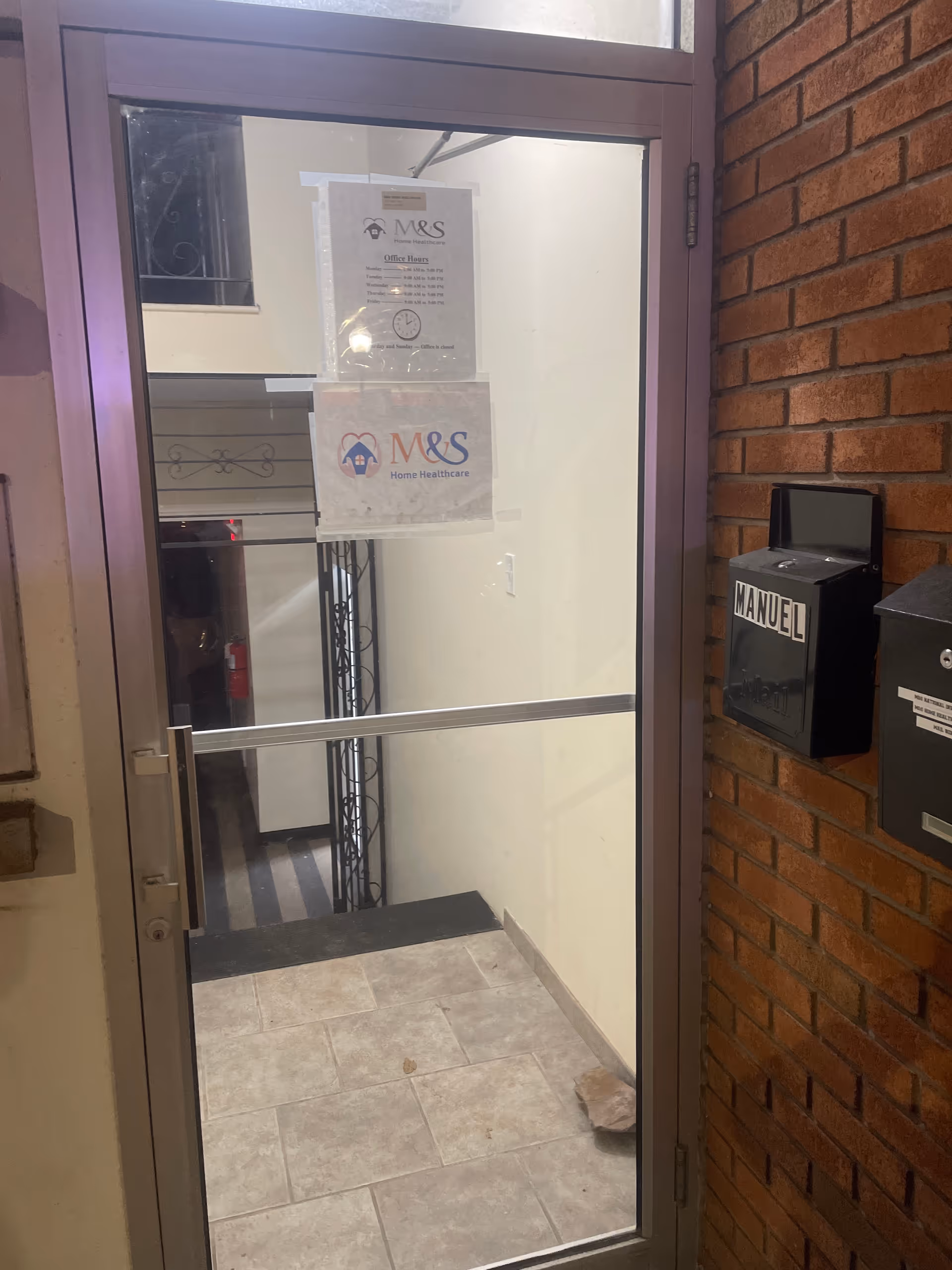 Glass door entry to a hallway with signs for M&S Home Healthcare and brick walls.