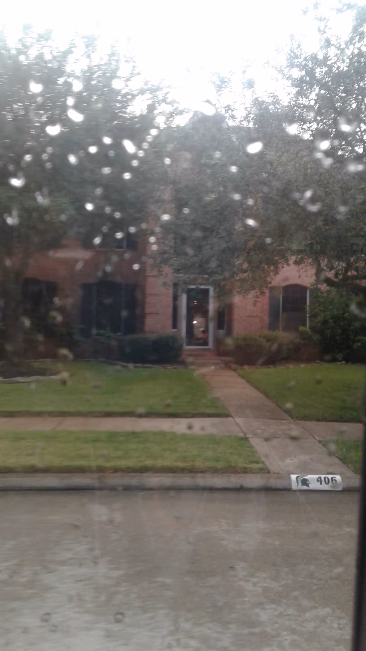 Rain-speckled glass frames a brick building entrance and sidewalk view.